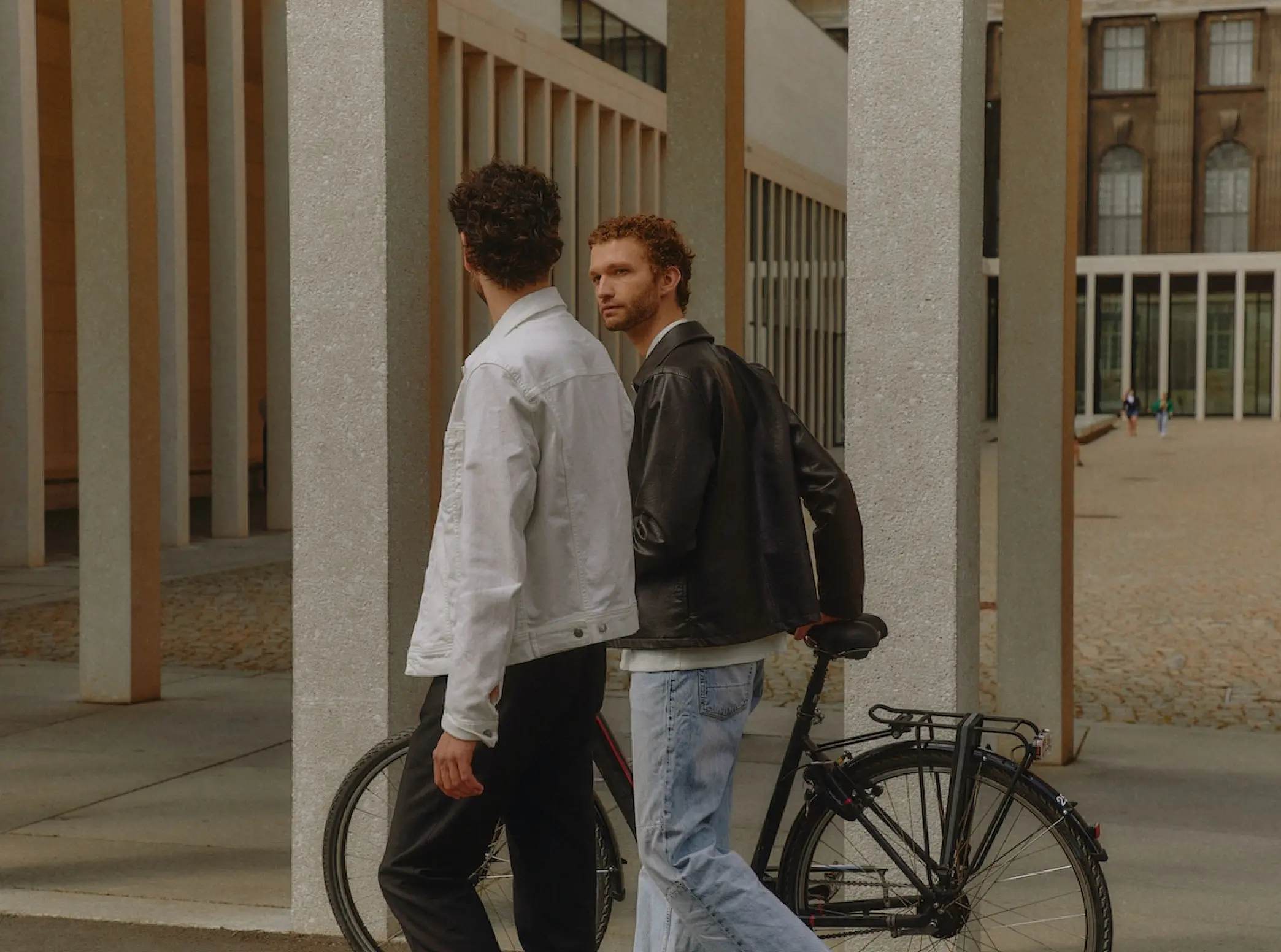 two men walking down a sidewalk next to a bike